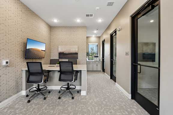 A room with a desk and chairs and a television on the wall.
