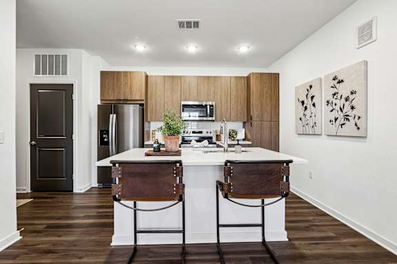 A kitchen with a white counter top and brown chairs.