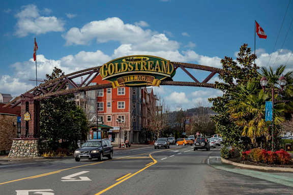 A street view of Goldstream Village with cars driving on the road.