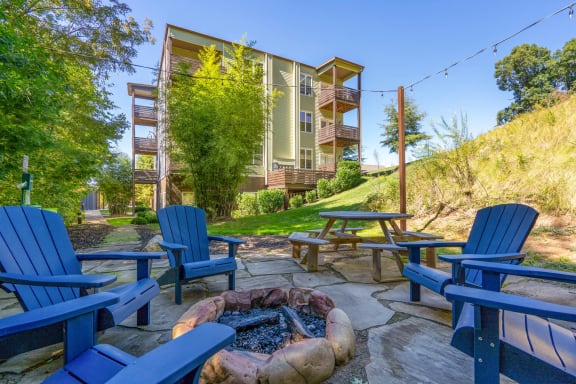 A fire pit is surrounded by blue Adirondack chairs in a backyard  at River Mill Lofts & Skyloft in NC 28803
