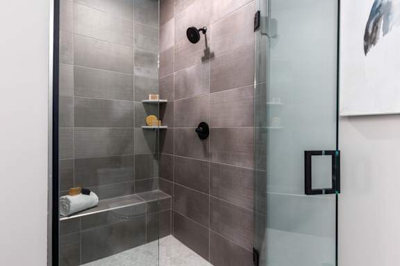 A modern bathroom with a glass shower door and grey tiles.