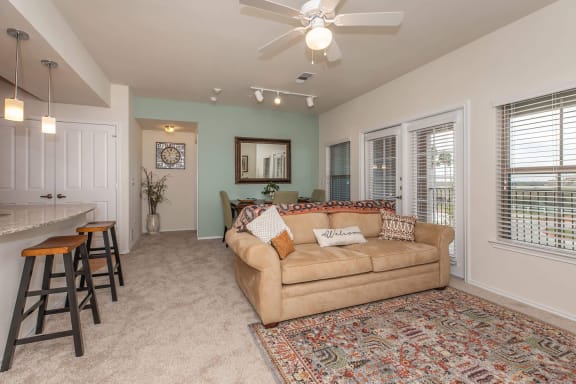 a living room with a couch and a kitchen with a bar at Mariposa at Clear Creek Webster 55+ Apartments, Webster, TX 77598