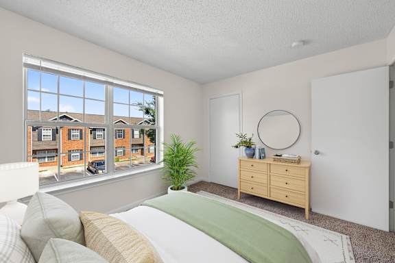 A bedroom with a large bed, a dresser, and a window overlooking a residential area.