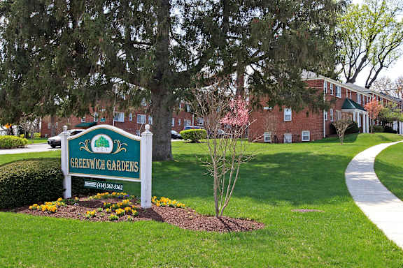 A sign for Oak Hill Apartments is displayed in front of a tree.