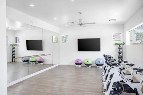 A gym with a row of exercise bikes and two television screens on the wall.