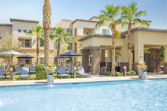 A pool surrounded by palm trees and lounge chairs.