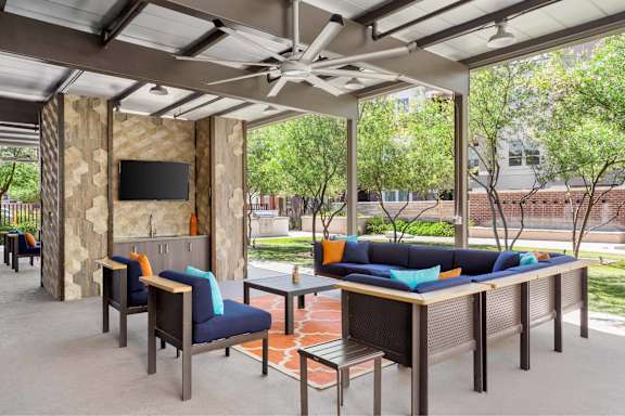 A patio with a couch, chairs, and a television.