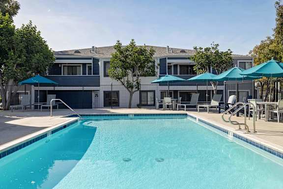 A swimming pool with a blue umbrella and a building in the background.