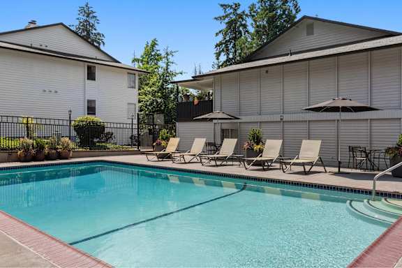 A pool with chairs and umbrellas in front of a house.