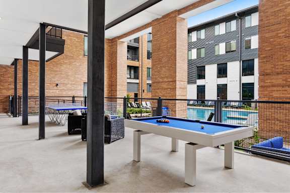 A pool table is surrounded by a black railing in a room with brick walls.