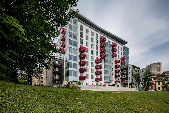 A modern building with red balconies is surrounded by greenery.