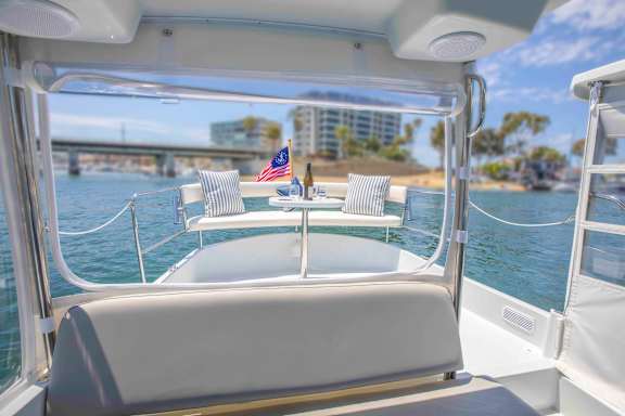 A boat with a white interior is docked in a body of water with a city skyline in the background.