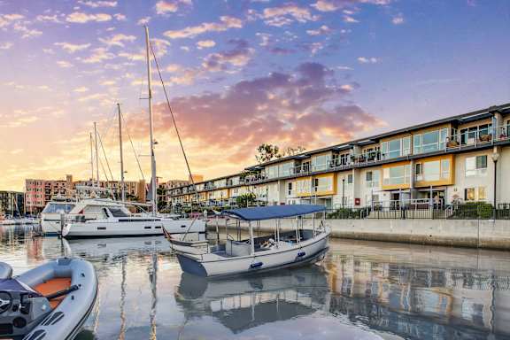 Boats are docked in front of a building with a sunset in the background.
