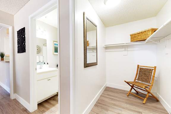 A white bathroom with a wooden chair and a mirror.