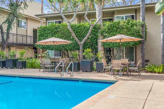 A pool surrounded by chairs and umbrellas in front of a building.
