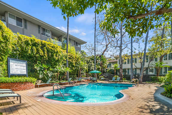 A pool surrounded by a wooden deck and green trees.