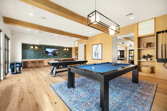 A pool table in a room with wooden floors and a television in the background.