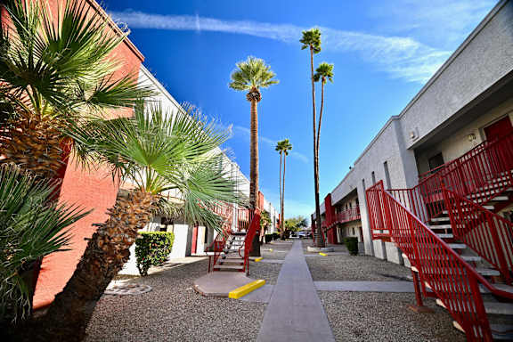 A pathway with red railings and palm trees.