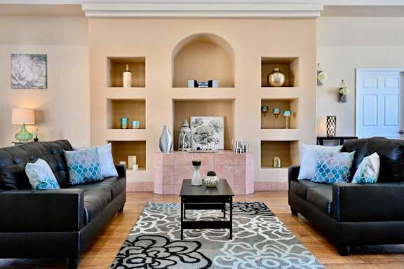 A living room with black leather couches and a patterned rug.
