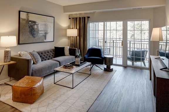 A living room with a grey couch, a coffee table, and a large window with curtains.