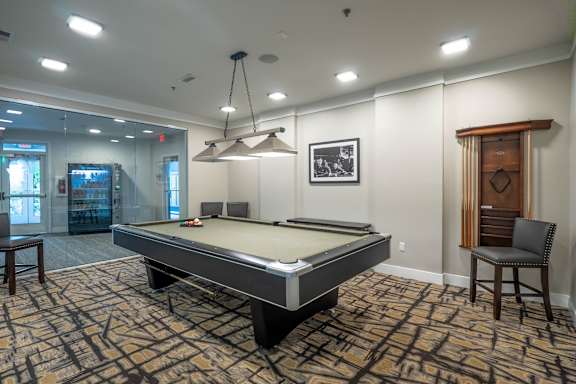 A pool table is in the middle of a room with a chair and a picture on the wall.