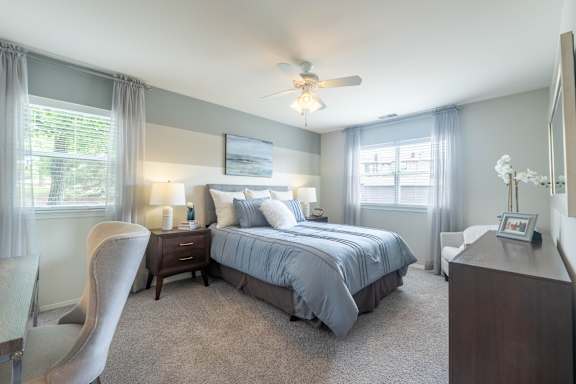 A bedroom with a bed, nightstand, chair, and a ceiling fan.