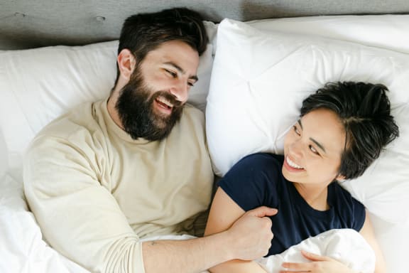 a couple laying in bed and smiling at each other