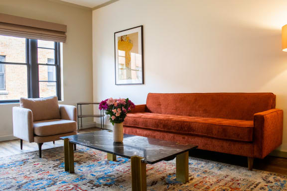 Living Room With Plenty Of Natural Light with a couch and a table with flowers  at The James – Furnished Apartments, California