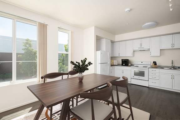 A dining table with chairs and a potted plant sits in a kitchen.