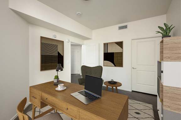 A laptop is open on a wooden desk with a cup and saucer, a plant, and a chair in a room.