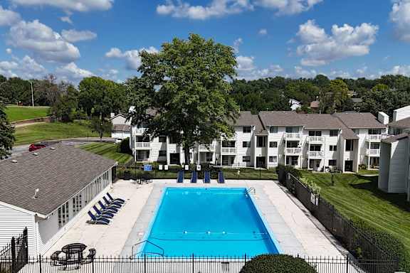 A swimming pool surrounded by a fence and chairs with apartment buildings in the background.