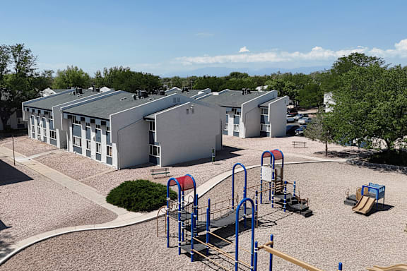 A playground with a slide, swings, and monkey bars in front of a building.