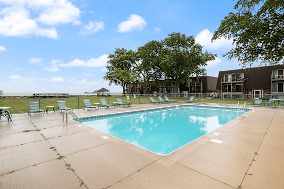 A large outdoor swimming pool surrounded by lounge chairs and trees.