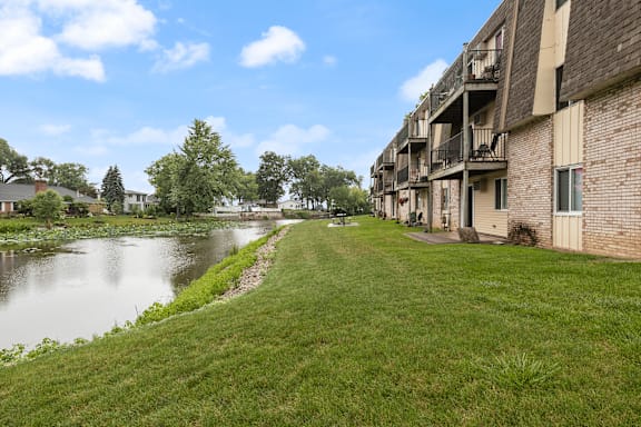 A river runs through a grassy area next to apartment buildings.