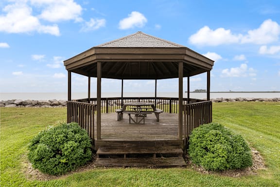 A wooden gazebo with a bench and two bushes in front of it.