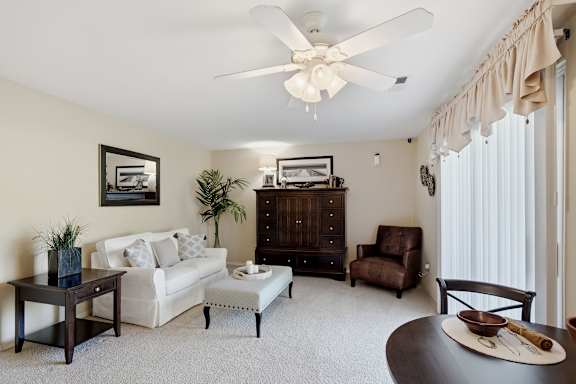 A living room with a white couch, a coffee table, a side table, a chair, a cabinet, and a ceiling fan.