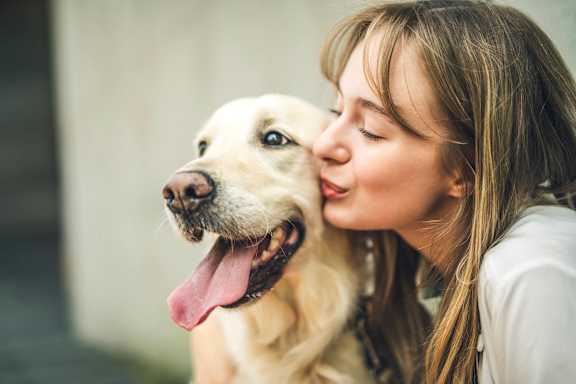 A woman is kissing a happy dog on the cheek.