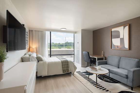 A modern bedroom with a large bed, a grey sofa, and a flat-screen TV mounted on the wall.