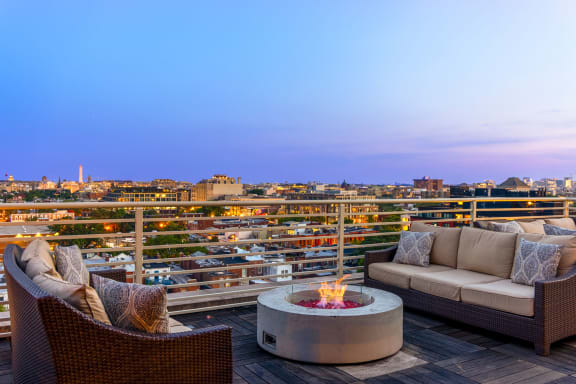 a rooftop deck with couches and a fire pit overlooking a city at night