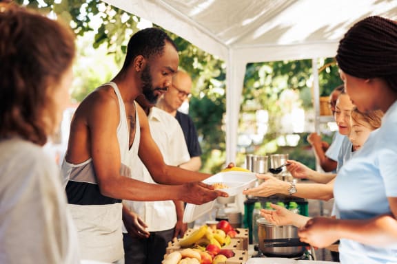 a group of people standing around a table with vegetables and bottles of ketchup