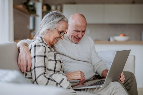 an older couple sitting on a couch looking at a laptop computer at Kirby Terrace Senior Apts, Hemet, 92545
