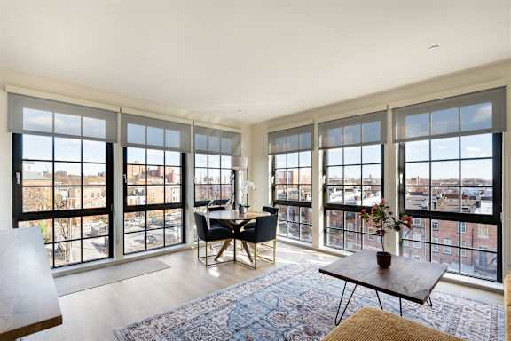 A white table with two chairs is in front of a window with a view of a city.