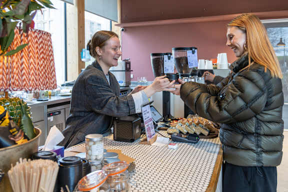 A woman in a black jacket is handing a card to another woman at a counter with a variety of items on it.