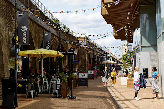 A street scene with people walking and sitting at tables under umbrellas.