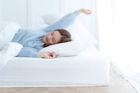 A woman in a blue shirt is stretching in bed.