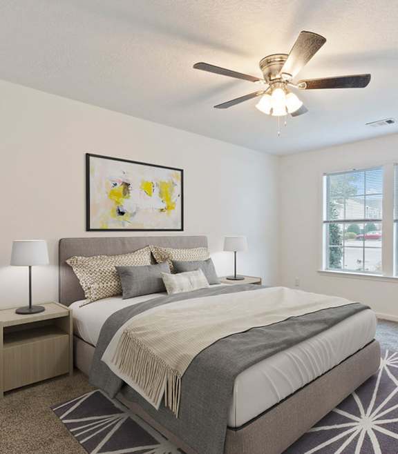 A bedroom with a large bed, a ceiling fan, and a chair.