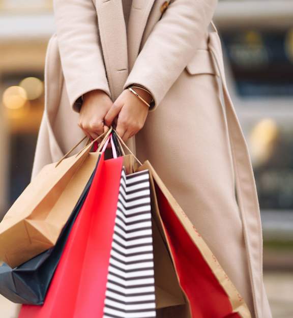 A person in a beige coat is holding shopping bags.