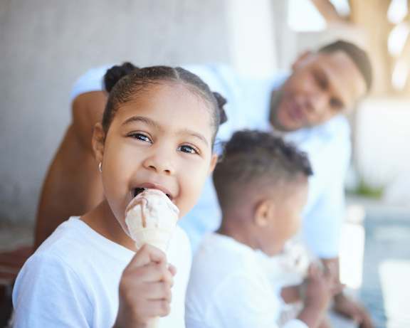 A young girl is eating an ice cream cone while two other children watch.