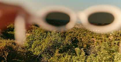 A person is wearing white sunglasses and looking at a landscape.
