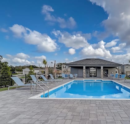 A swimming pool surrounded by lounge chairs and a building in the background.